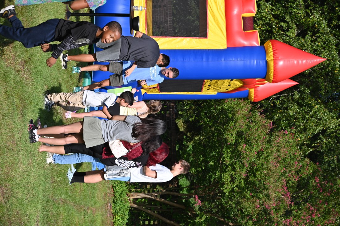 Kids and teens on the grass by a red, yellow, and blue bounce castle.